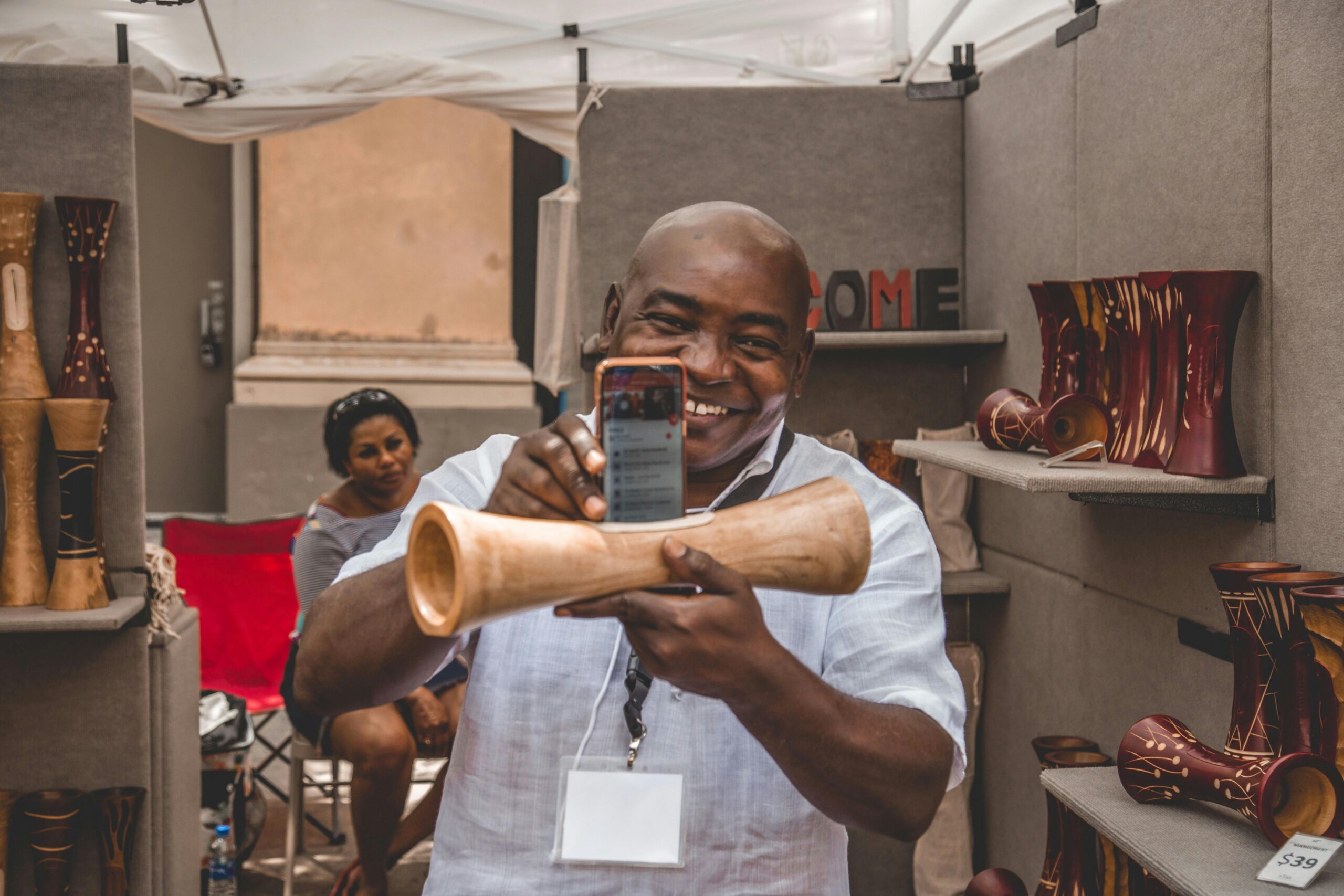 A cheerful artisan showcasing a handmade wooden piece at an indoor craft market.