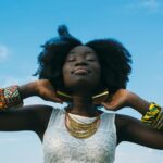 Portrait of a joyful African woman with afro hair, wearing colorful bracelets and gold earrings, enjoying the sunny day.